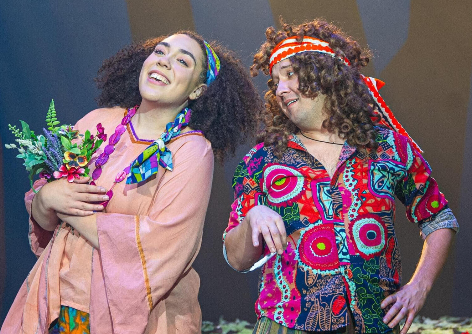 A Midsummer Night's Dream (2022, Nevada Conservatory Theater) A fairy from A Midsummer Night's Dream and Puck conversating and smiling in 1970's clothing.